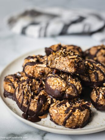 A plate of samoas cookies dipped in chocolate and sprinkled with toasted coconuts. There is a bit on top.