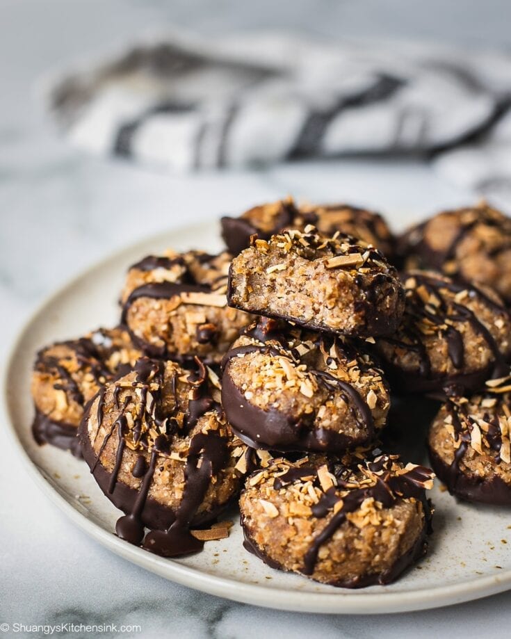 A plate of samoas cookies dipped in chocolate and sprinkled with toasted coconuts. There is a bit on top.
