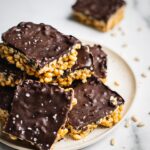 A plate of peanut butter chocolate rice krispie treats. There are sea salt on top of the chocolate layer.