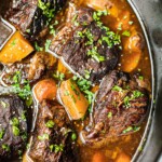 A crockpot full of Korean beef short ribs, potatoes, and carrots. It is garnished with cilantro.