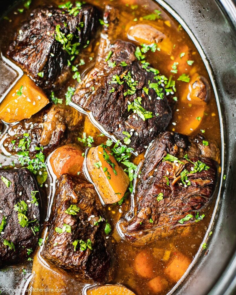 En crockpot fuld af koreansk oksekød med short ribs, kartofler og gulerødder. Den er garneret med koriander.