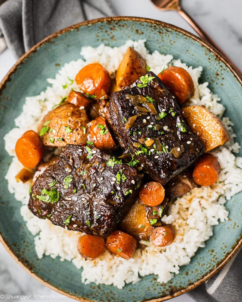 En tallerken med slow cooker koreanske short ribs serveret med jasminris. Der er gulerødder, kartofler i og garneret med koriander..