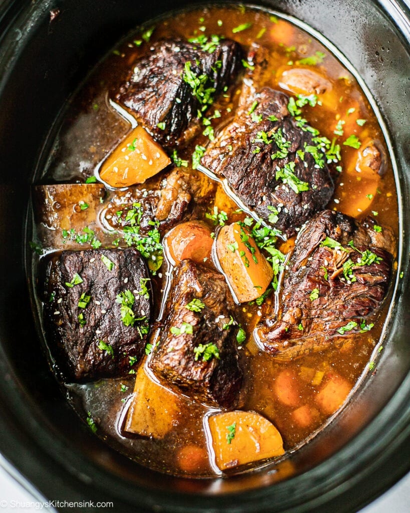 En crockpot fuld af koreanske oksekød short ribs, kartofler og gulerødder. Den er garneret med koriander.