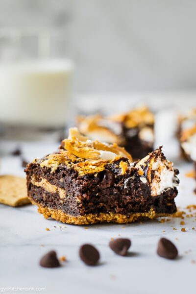 A piece of S'mores Brownie with graham cracker crust on the bottom, marshmallow and graham cracker on top. There is a bite in the middle.