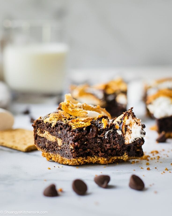 A piece of S'mores Brownie with graham cracker crust on the bottom, marshmallow and graham cracker on top. There is a bite in the middle.