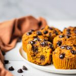 A plate of vegan whole wheat pumpkin muffins. The middle one has a bite in it. The most Moist and fluffy pumpkin muffin this fall.