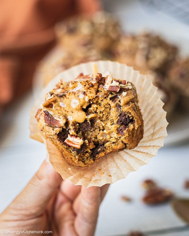 Freshly baked sweet potato muffin batter, half topped with chopped pecans on a plate. There is a bite in the middle of it, topped with nut butter.