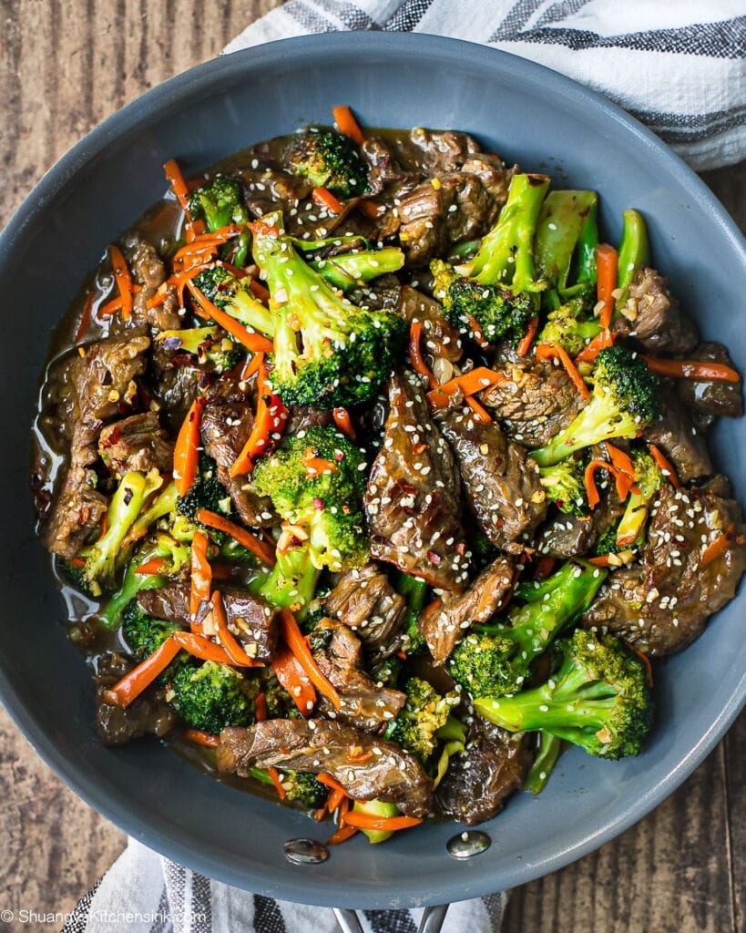 A pan of beef and broccoli stir fry with carrots and sesame seeds on top.