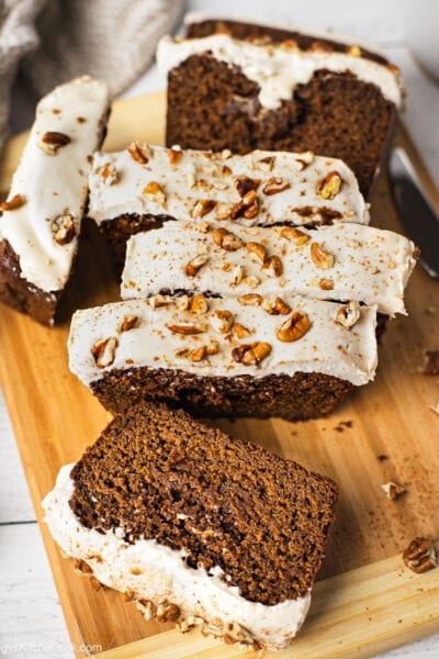 A loaf of slice paleo ginger bread loaf topped with cashew cream cheese frosting that makes it healthy and dairy free. There are pecan pieces on top of the gingerbread loaf.
