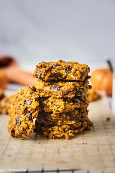 A stack of pumpkin oatmeal chocolate chip cookies. There is one oatmeal cookie leaning on the stack of the stack of cookies.