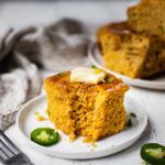 A slice of honey jalapeños cornbread that is gluten free and dairy free. Optional toppings to make it a delicious honey butter cornbread. There is another plate of cornbread in the back.