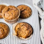 A batch of freshly homemade gingerbread muffins topped with powdered sugar. There is a bite in this whole wheat muffin, and the texture appears to be soft and gooey.