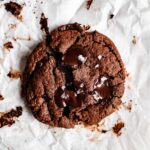 A piece of paleo chocolate cookie with a split in the middle. There are melty chocolate chips on top with a sprinkle of sea salt.