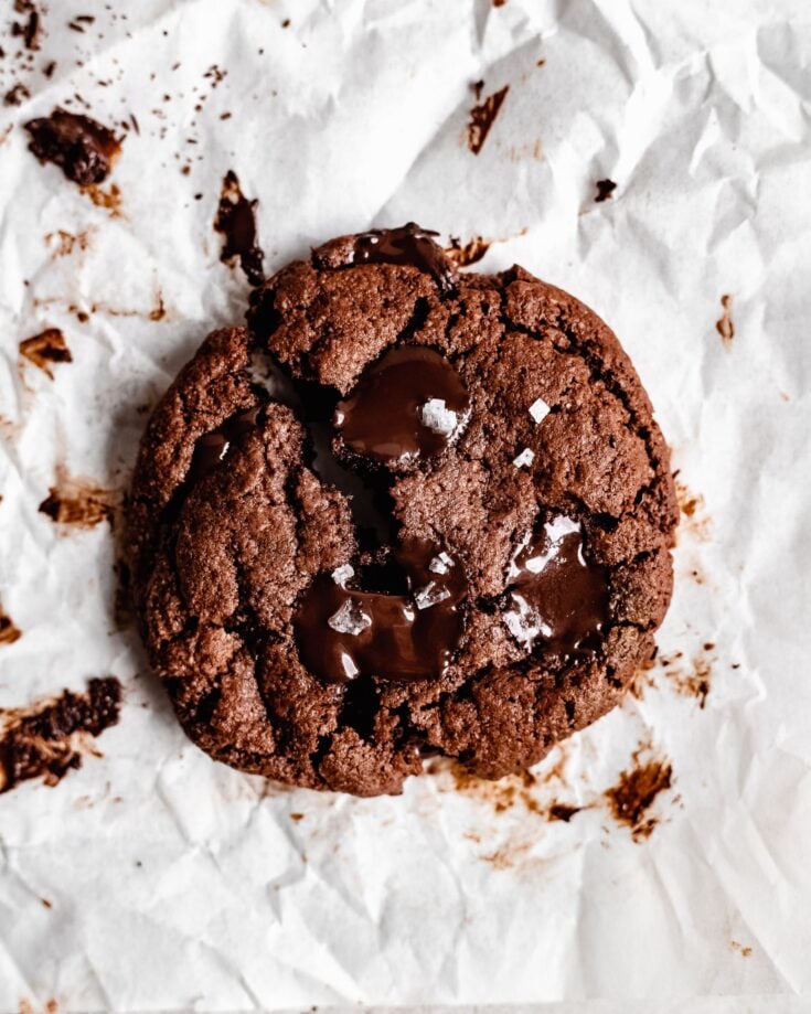 A piece of paleo chocolate cookie with a split in the middle. There are melty chocolate chips on top with a sprinkle of sea salt.