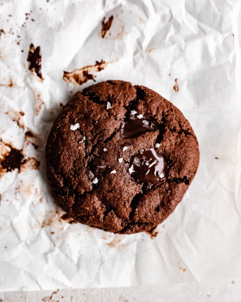 Um pedaço de biscoito de chocolate paleo com uma divisão no meio. Há pedaços de chocolate derretido por cima com um sal grosso.