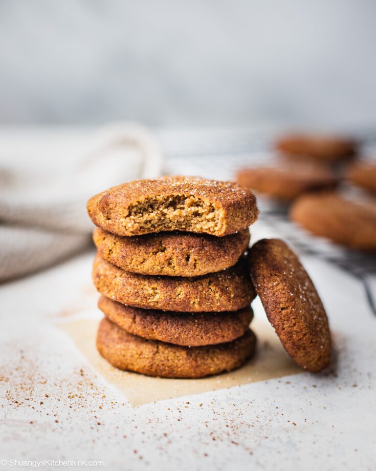 A batch of keto snickerdoodles pm a board. They are coated with cinnamon sugar. There is a bite on one snickerdoodle cookie. The texture appear to be soft and chewy.