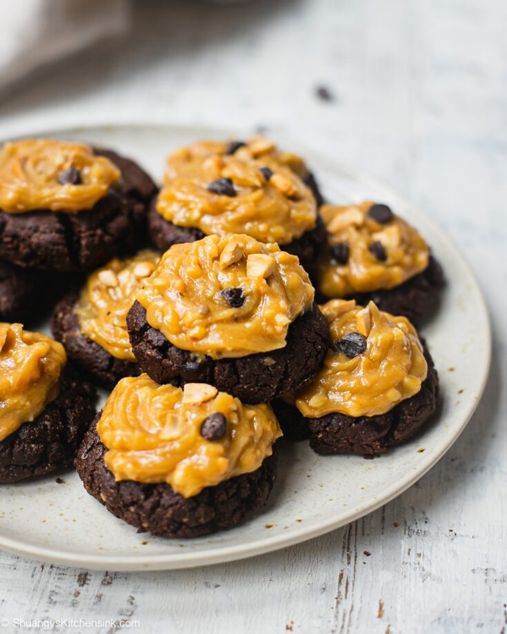A batch of paleo and vegan chocolate cookies topped with 3-ingredient peanut butter frosting. There are dark chocolate chips on top of the peanut butter frosting.