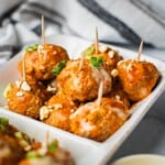 A serving dish of healthy buffalo chicken meatballs topped with scallions, blue cheese and ranch dressing.