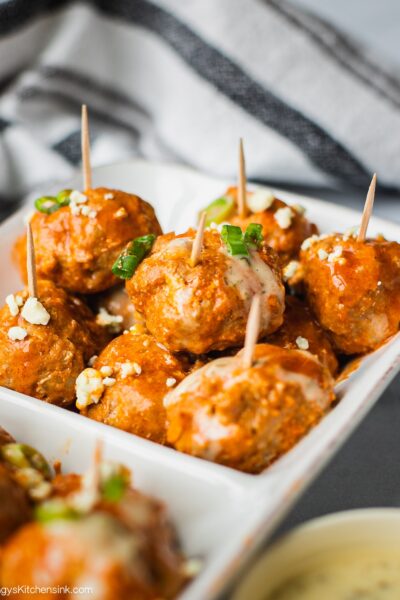 A serving dish of healthy buffalo chicken meatballs topped with scallions, blue cheese and ranch dressing.