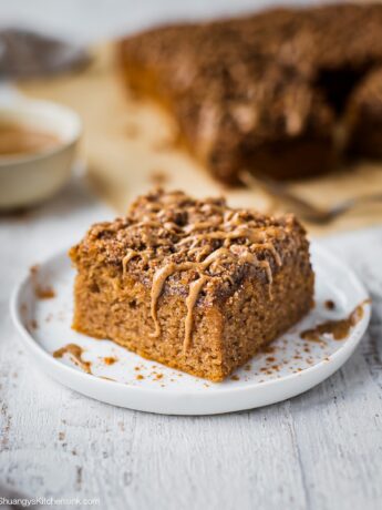 A piece of gluten free coffee cake topped with gluten free crumble toppings. There is the rest of the healthy coffee cake in the background.