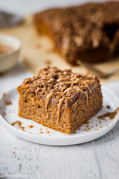 A piece of gluten free coffee cake topped with gluten free crumble toppings. There is the rest of the healthy coffee cake in the background.