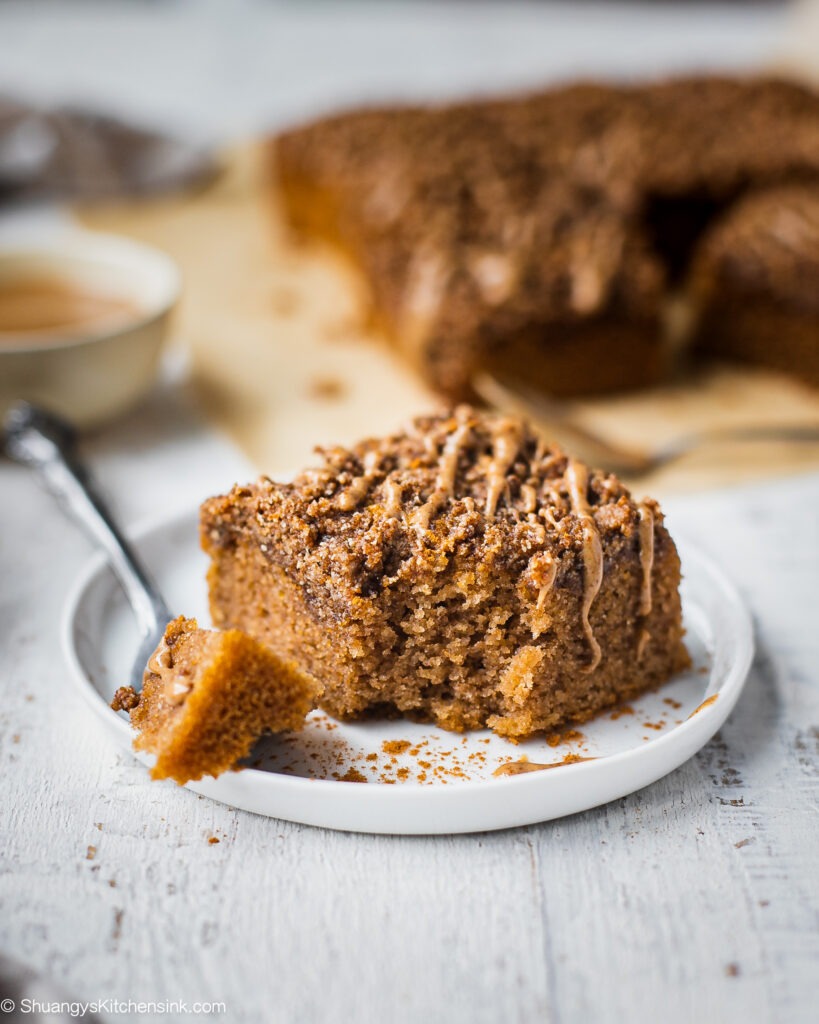 A piece of gluten free coffee cake with cinnamon crumble toppings on a plate. There is a fork with a bite on the healthy coffee cake.