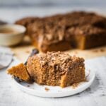 A piece of gluten free coffee cake with cinnamon crumble toppings on a plate. There is a fork with a bite on the healthy coffee cake.