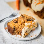 A piece of carrot cake banana bread with cashew cream cheese frosting that is dairy free. This carrot cake loaf recipe is paleo, gluten free and easy to make.