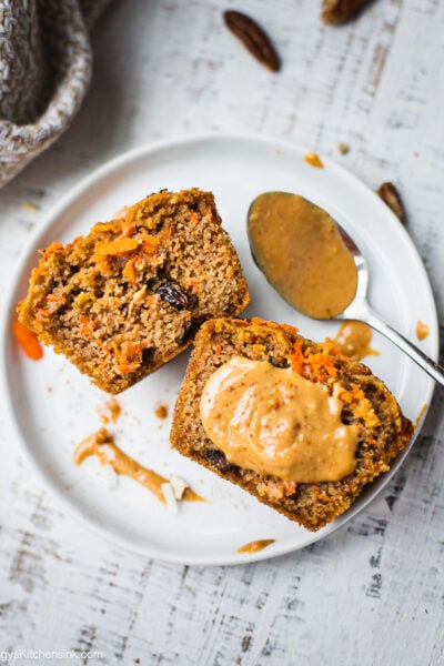 A gluten free carrot cake muffin cut in half. Half of the carrot muffin is topped with almond butter which makes a great healthy breakfast option.