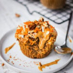 A gluten free carrot cake muffin cut in half. Half of the carrot muffin is topped with almond butter which makes a great healthy breakfast option.