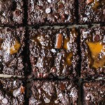 A batch of caramel swirl brownies on a piece of parchment paper. The grain free brownie base are topped with healthy caramel and sea salt.