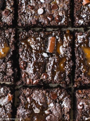 A batch of caramel swirl brownies on a piece of parchment paper. The grain free brownie base are topped with healthy caramel and sea salt.