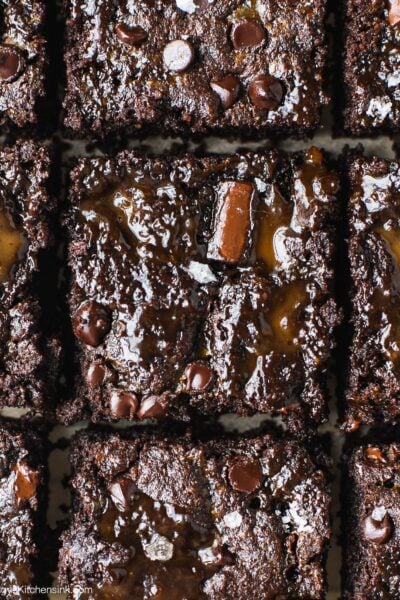 A batch of caramel swirl brownies on a piece of parchment paper. The grain free brownie base are topped with healthy caramel and sea salt.
