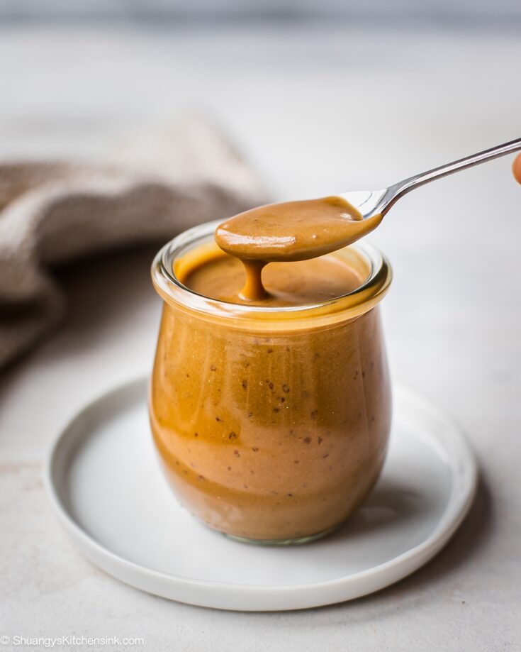 A jar of vegan caramel sauce with a spoonful of it coming out of the jar. The texture appears to be thick and velvety and the color is golden brown.