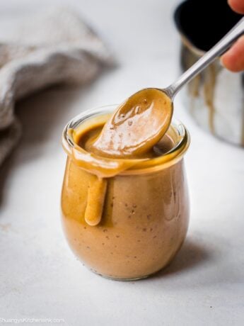 A jar of keto caramel sauce on a plate. There is a drip of the healthy caramel sauce on the side of the jar.