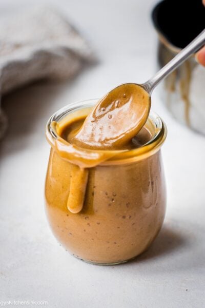 A jar of keto caramel sauce on a plate. There is a drip of the healthy caramel sauce on the side of the jar.