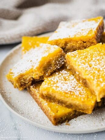 A plate of gluten free lemon bar that has powdered sugar on top and a bite in the middle. The texture appears to be creamy and soft.