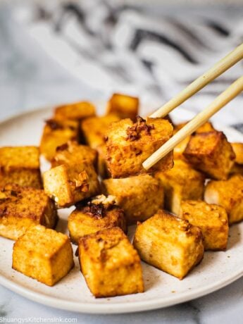 A plate full of air fried crispy tofu. One piece is being picked up by chopsticks