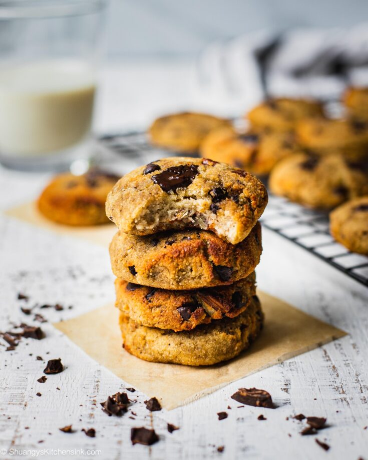 four banana bread cookies are stacked on top of each other in front of more gluten free cookies . Someone has already taken a bite from the top cookie