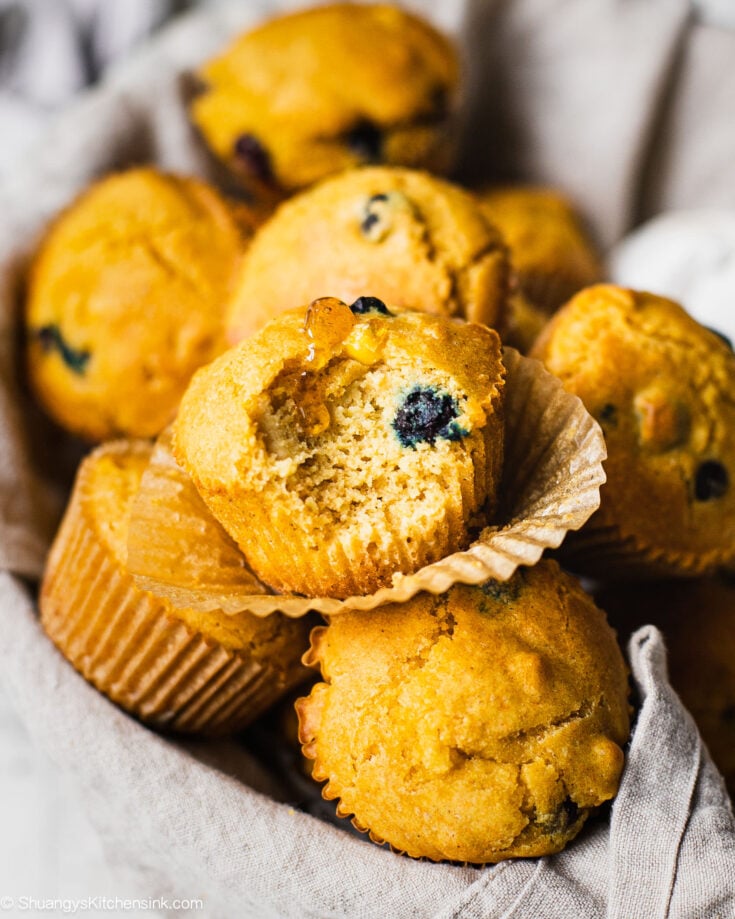 There are many cornbread muffins. Someone has taken a bite from he one in the front. There is honey drizzled on the dessert