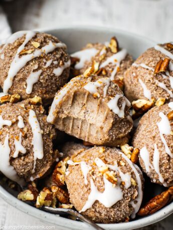 A Serving ball filled with raw cinnamon roll cookies that has been drizzled with healthy coconut butter and toasted pecans. Someone has taken a bit from one off the balls.
