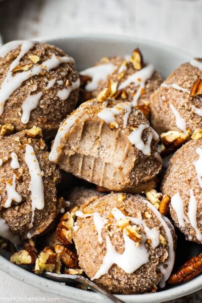 A Serving ball filled with raw cinnamon roll cookies that has been drizzled with healthy coconut butter and toasted pecans. Someone has taken a bit from one off the balls.