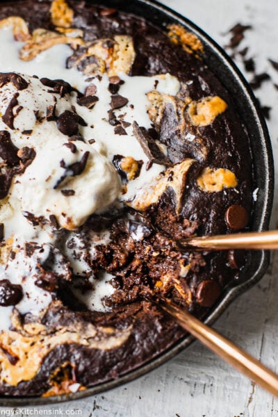 A cast iron skillet of healthy brownie topped dark chocolate chips and vanilla ice cream.