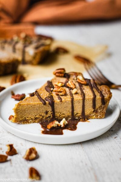 There is a piece of no bake pumpkin cheesecake on a round plate. It's drizzles with homemade chocolate ganache and walnuts are sprinkled on top