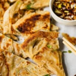 A Chinese Scallion Pancake cut into smaller wedges. There is a pipping sauce on the side and chopsticks.