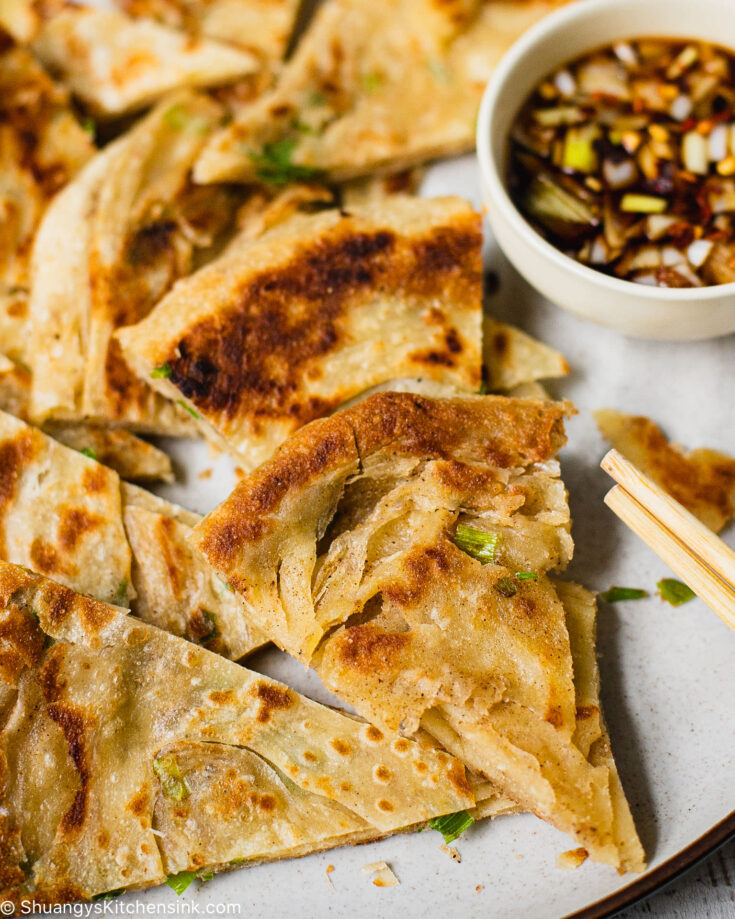 A Chinese Scallion Pancake cut into smaller wedges. There is a pipping sauce on the side and chopsticks.