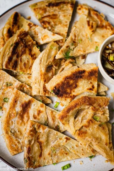 A Chinese Scallion Pancake cut into smaller wedges. There is a pipping sauce on the side and chopsticks.