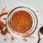 A bowl with BBQ spices mixed togeter with a spoon that's laying next to the bowl