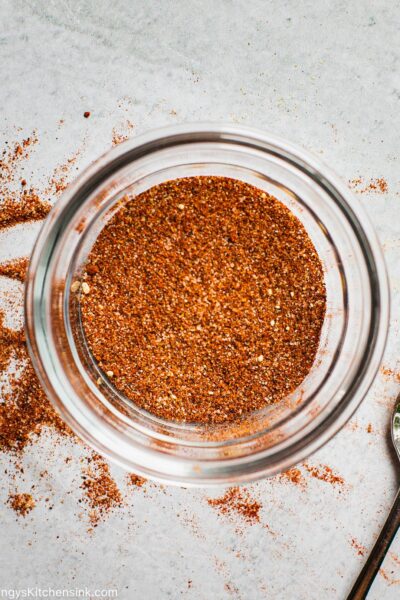 A bowl with BBQ spices mixed togeter with a spoon that's laying next to the bowl