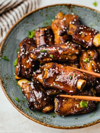A pair of chopsticks are grabbing a short rib covered in a sticky Asian sauce